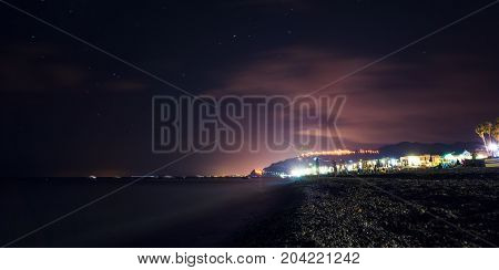 Clear summer night over the sicilian coast Furci Siculo Italy. The lights create dramatic colors over the sea