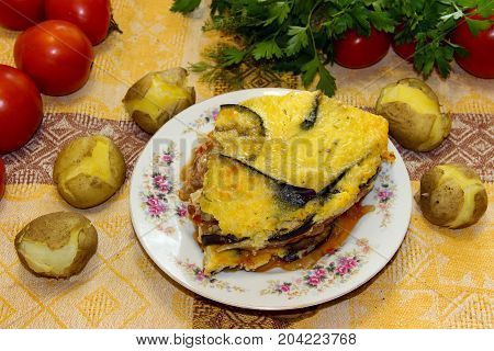 Hot Ready Moussaka Is Served On A Porcelain Plate Among Vegetables And Spicy Herbs. Fresh Vegetables