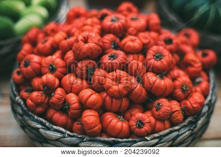 Wicker wooden basket full of slightly flaccid ripe red eggplant (Solanum aethiopicum) after autumn harvesting looking like tomatoes; shallow depth of field