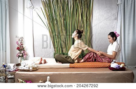 Thai Masseuse doing massage for woman in spa salon. Asian beautiful woman getting thai herbal massage compress massage in spa.She is very relaxed. Healthy Concept