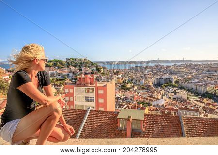 Aerial view of Lisbon, Portugal, from the highest point in the city. Caucasian woman looking Lisbon panorama from viewpoint Our Lady of Mt. in Alfama district at sunset. Tourism and travel concept.