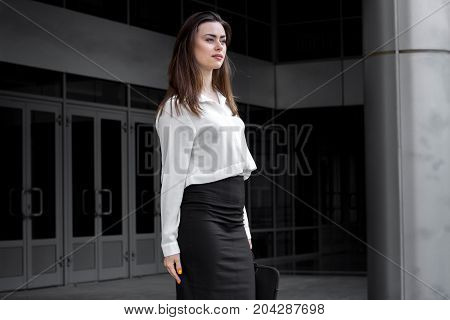attractive young business girl stands on a street in a white shirt and black skirt