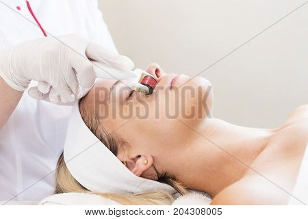 The woman undergoes the procedure of medical micro needle therapy with a modern medical instrument derma roller.