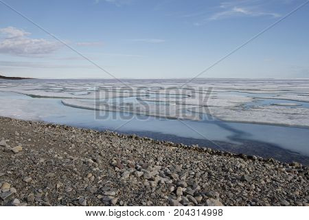 Broken pans of sea ice on ocean coast with blue sky and pebble beach along the Northwest Passage