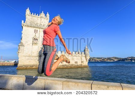 Happy blonde caucasian woman jumping at Belem Tower, Unesco Heritage and symbol of Lisbon, in Belem District, Tagus River. Lifestyle traveler female enjoying Torre de Belem. Freedom and travel concept