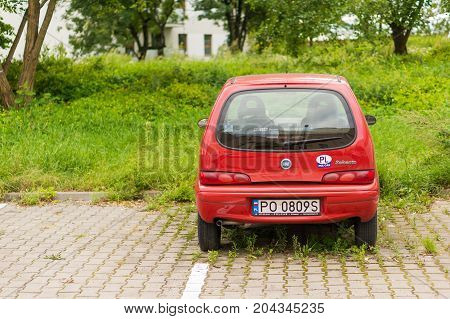 Red Fiat Seicento parked on a parking spot with green weeds on August 2017 in Poznan Poland