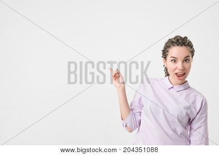 Shocked caucasian woman with braids hairstyle and good mood showing with index finger aside. Copyspace for text