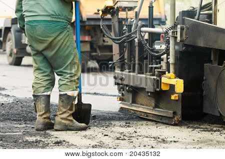 Trabajador operando la máquina pavimentadora de asfalto durante la construcción de carreteras y obras de reparación