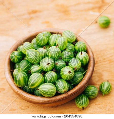 Old Wooden Bowl Filled With Succulent Juicy Fresh Ripe Green Gooseberries On An Old Wooden Table Top.