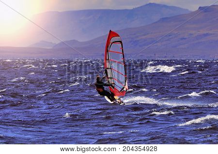 Sportman windsurfer on the lake surface at sunset time.