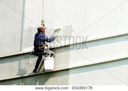 painter person hanging on white building .