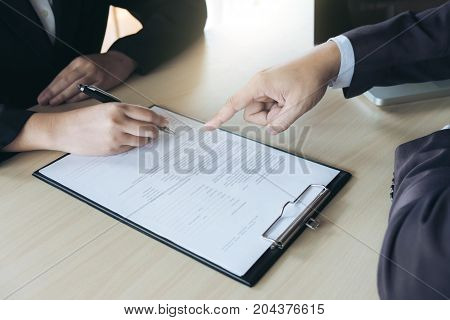 Closeup of woman applicant writing in resume form person completing filling information and executive pointing help her to sign in application form hiring concept.