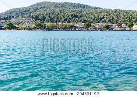 Low angle view on the stony beach with beautiful shallow turquoise water and town over sea.