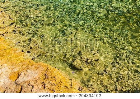 Rocky seafloor visible through crystal clear turquoise transparent rippling water.