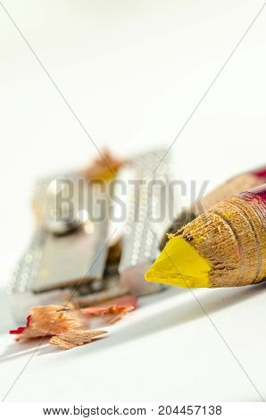colored pencils sharpened with a pencil sharpner in the background. school.