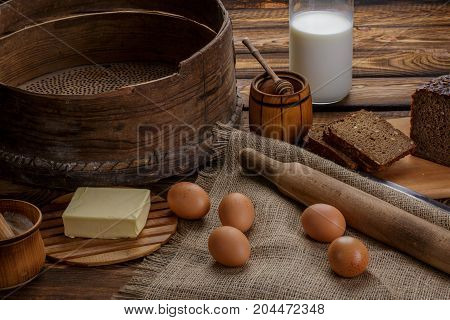 Ingredients for cooking eggs honey bread flour and milk over sackcloth or burlap and wooden background