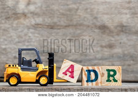 Yellow plastic forklift hold letter A to complete word ADR (Abbreviation of Adverse drug reaction) on wood background