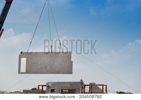 Construction site crane is lifting a precast concrete wall panel to installation building.