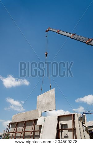 Construction site crane is lifting a precast concrete wall panel to installation building.