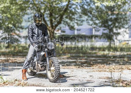 Cool looking motorcycle rider on custom made scrambler style cafe racer in the park