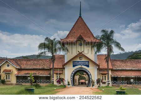 MYsore India - October 27 2013: Horseshoe-shaped entrance gate and historic yellow red tiled building of Mounted Police headquarters stands in park with green lawn and trees. Guard officers in front. Bluish sky.