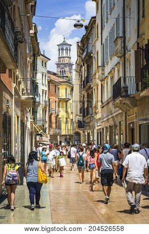 VERONA ITALY - JUNE 25 2016: Picture from Via Giuseppe Mazzini with many stores and tourists with Torre dei Lamberti in the background in a sunny day with clouds. Verona Italy.