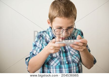 Handsome boy in glasses plays tablet. The concept of poor eyesight harm of gadgets myopia