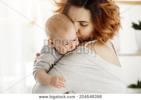 Young good looking mother hugs and calms her crying baby. Child screaming and crying on mother shoulder. Scene of protection and love. Family concept