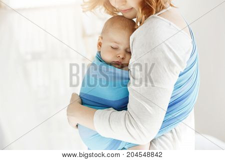Tiny newborn child close eyes and having good sleep in baby slim feeling protection from his beautiful young mother. Family, lifestyle concept