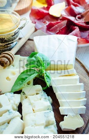 Cheese platter: Brie Parmesan cheddar gouda gorgonzola and other with walnuts and honey on wooden board. Tasty appetizers with different kind of cheese. Delicious snack on party or picnic time.