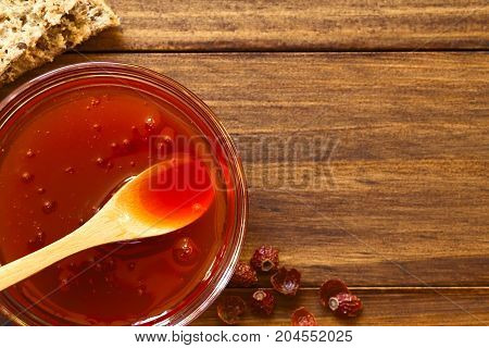 Homemade rose hip jam in glass bowl with wooden spoon photographed overhead on wood with natural light (Selective Focus Focus on the top of the jam)