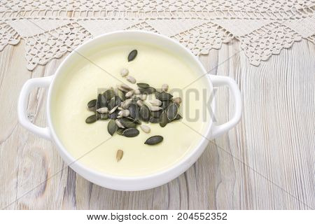 Tasty potato soup and handmade crochet napkin on rustic wooden table. Traditional lunch or dinner. Potato and onion vegan vegetarian healthy cream soup with pumpkin and sunflower seeds white bowl