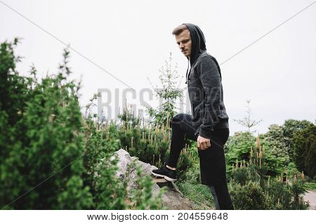 A well built guy is standing on the stone with the right leg and having some rest after a big running distance. he is analyzing his path and trying to make concequences from it.