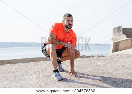 Portrait of pensive young handsome strong man wearing sportswear, looking away and sitting on hunkers with river in background