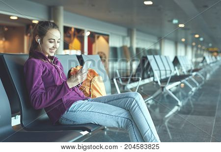 Girl at the airport window sits on the banch and looking at smartphone