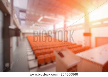 Abstract blur Rostrum with microphone and computer in conference hall. Orange color.
