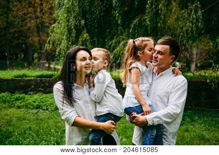 family of four people portrait in city park kids kissing perents