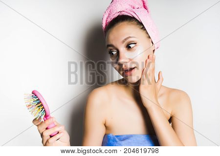 Young beautiful woman with a mask under the eyes looks at herself in the mirror