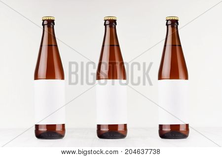 Three brown NRW beer bottles 500ml with blank white label on white wooden board mock up. Template for advertising design branding identity.