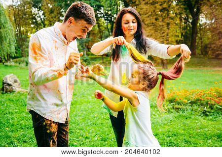 father mother and daughter full around with holi paints in city park