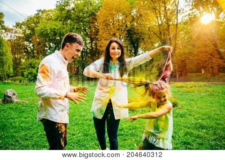 father mother and daughter full around with holi paints in city park