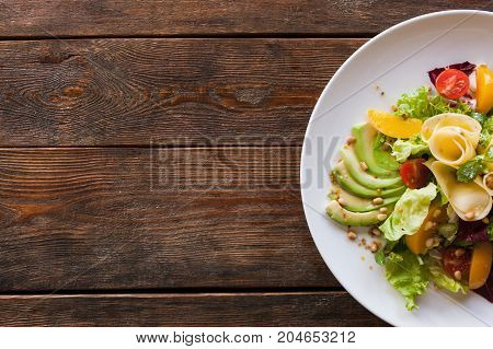 Lettuce salad with cheese and fruits on plate. Fresh vegetables decorated pine nuts, avocado, pearch and pear, serving in restaurant, top view with free space on left