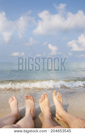 Two people legs on sea beach. Blue sky with clouds
