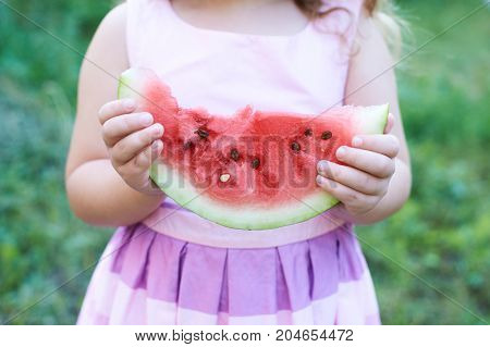 Little girl holding red watermelon piece. Dress