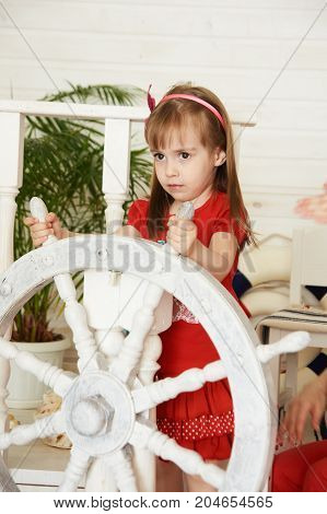 Young girl driving white steering wheel. Red dress