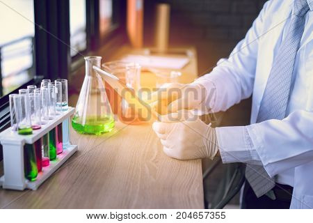 Scientist man with glasses working tablet reserch and conducts experiments by synthesising compounds in laboratory and the test tube