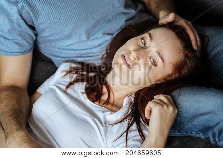 Too much stress. Sad cheerless red haired woman lying on her boyfriends legs and thinking about her problems while being stressed out
