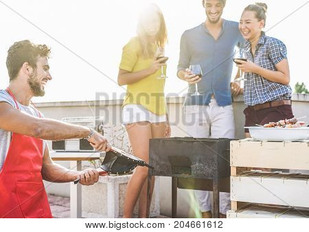 Group of friends having fun at rooftop barbecue party - Happy chef making fire with bellows for bbq dinner - Focus on left man - Youth food friendship concept - Original color sun tones editing