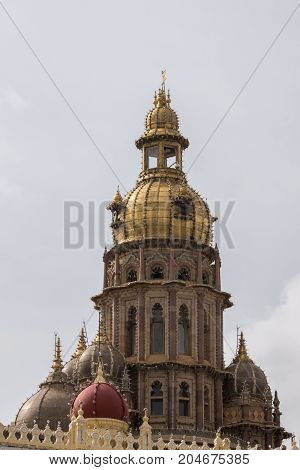 Mysore India - October 27 2013: closeup of central tower with golden domes of Mysore Palace. Lines of light bulbs brown stones and more smaller domes against gray sky.