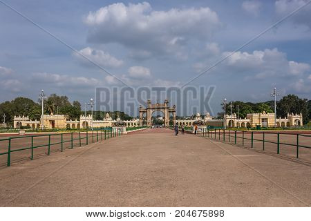 Mysore India - October 27 2013: Brown stone main East Gate to Mysore Palace with entire yellow side buIldings under cloudscape. Visitors add colors.